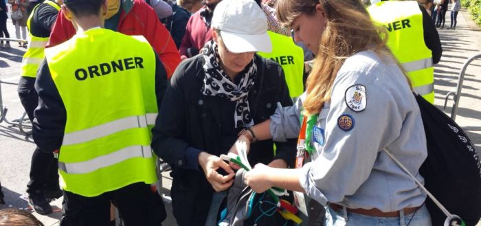 Kirchentag: Eine Pfadfinderin befestigt nach der Taschenkontrolle ein Bändchen an den Rucksack einer Besucherin