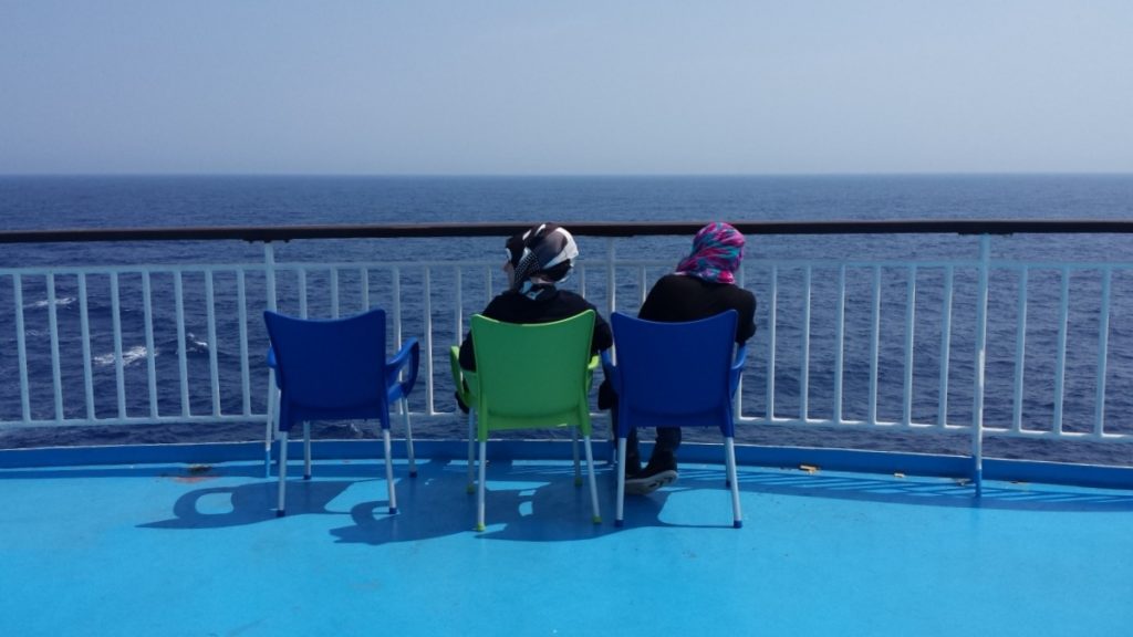 Zwei Frauen sitzen auf Stühlen an der Reeling und schauen aufs Meer