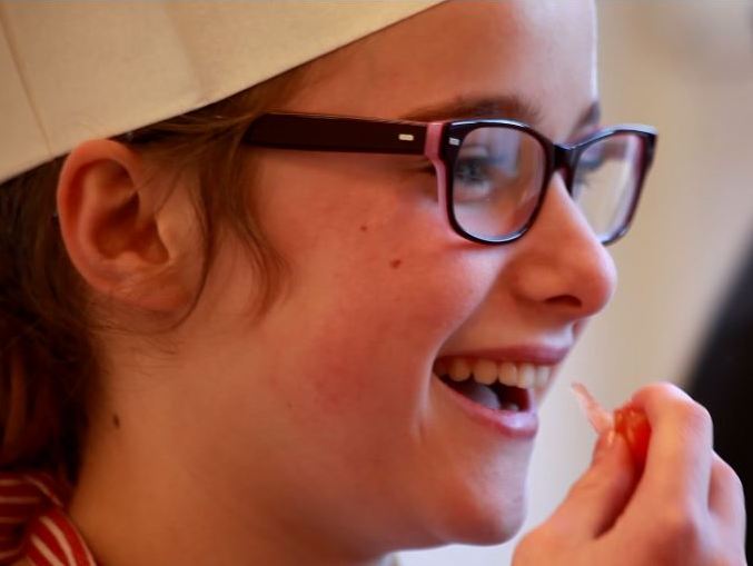 Mädchen mit Kochmütze probiert lachend ein Stück Paprika