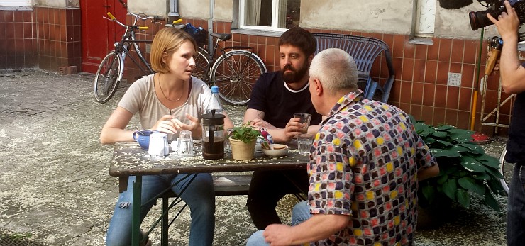 Eine Frau und zwei Männer sitzen um einen Tisch im Hof ihres Mietshauses beim Dreh über die Mietwohnungsmisere für das ZDF