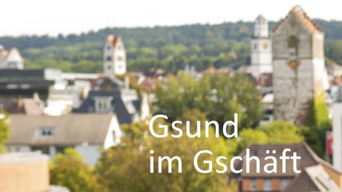 Schrift "Gsund im Gschäft" - schwäbische Schreibweise - vor der verschwommenen Stadtkulisse Ravensburg