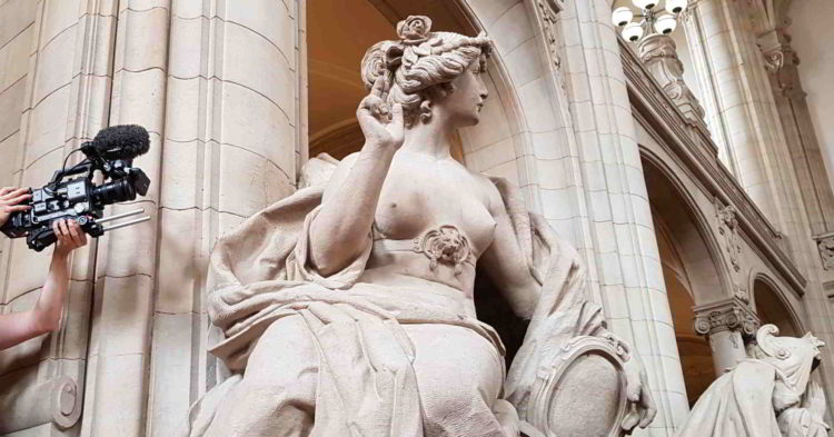 Halbnackte Frauenfigur aus Stein erhebt die rechte Hand zum Schwur, links von ihr ist eine Videokamera zu sehen